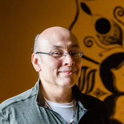 A man with glasses and bald head standing in front of a wall.