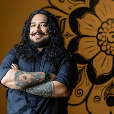 A man with long hair and tattoos standing in front of a wall.