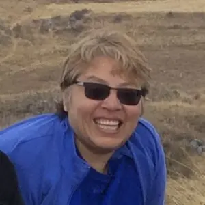 A woman in sunglasses and blue shirt smiling.